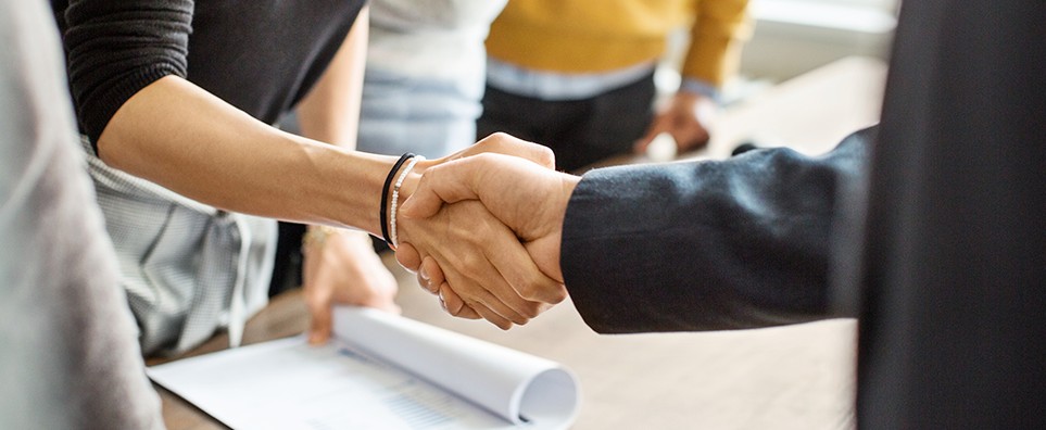 To personer giver hinanden hånd under et møde, som symbol på god service og et stærkt samarbejde.