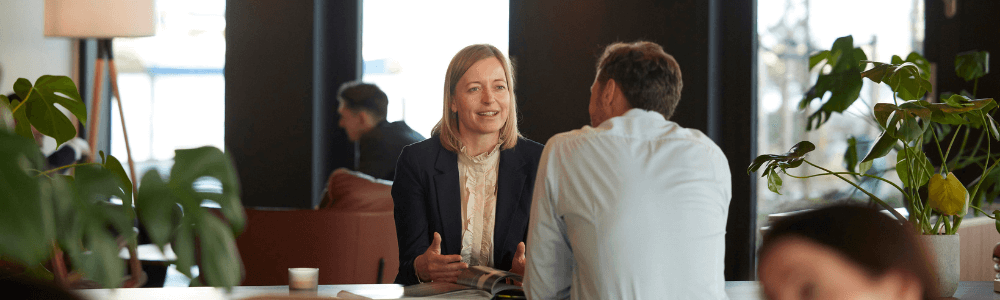 Talende kvinde sidder overfor for mand ved højt bord