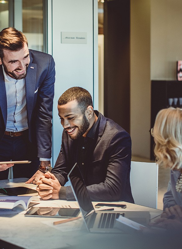 Kollegaer sidder samlet omkring et mødebord og diskuterer, mens en person forklarer noget til gruppen under et møde.