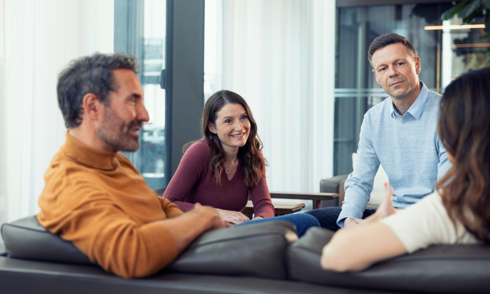 Fire personer sidder i sofa og kommunikerer Fire personer sidder i sofa og kommunikerer