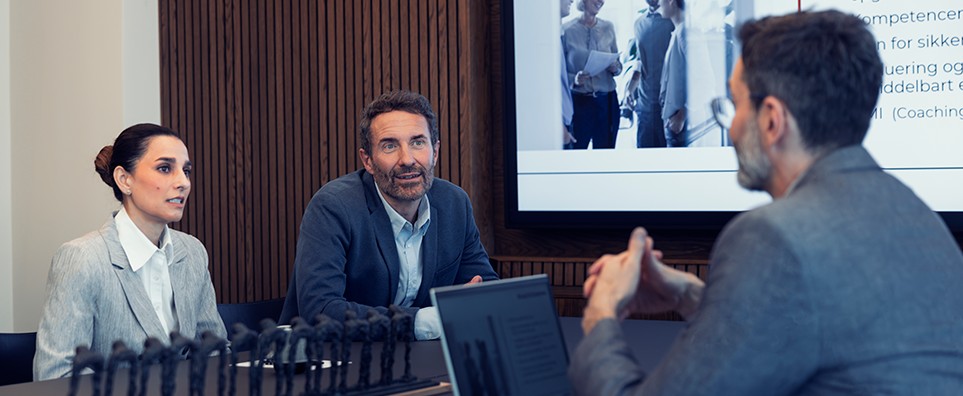 To medarbejdere præsenterer en løsning for en kunde under et møde om service og samarbejde.