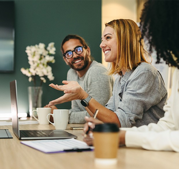 Tre kollegaer taler sammen ved et bord under et møde og udveksler idéer om service og samarbejde.